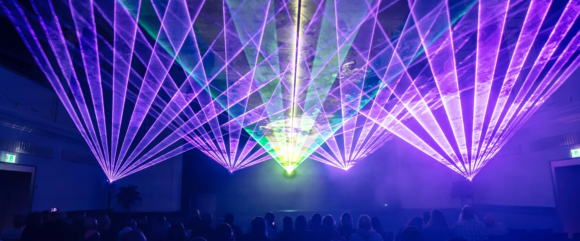 Lasershow bei einer Vernissage in Miesbach: violette Strahlenfächer über dem Publikum im Saal
